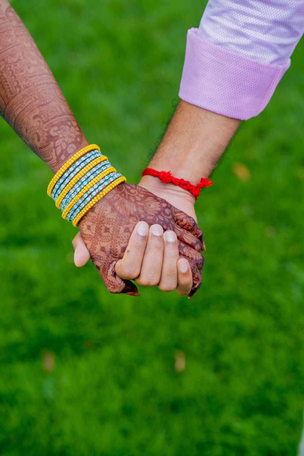 Close-up of bride and groom holding hands with bridal bangles and mehndi