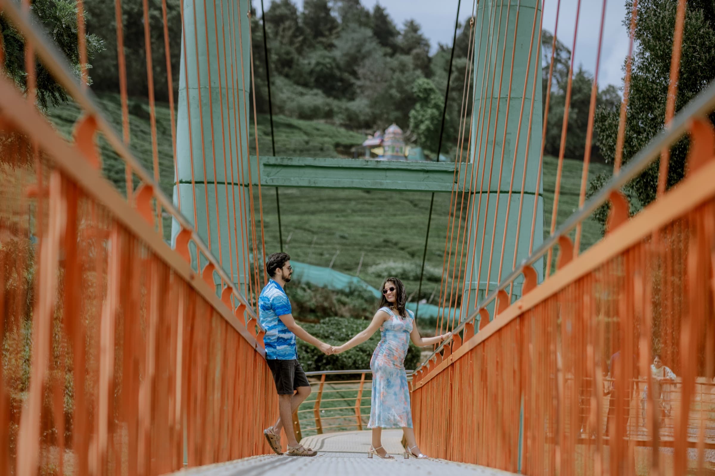 Couple holding hands on an orange hanging bridge in the hills