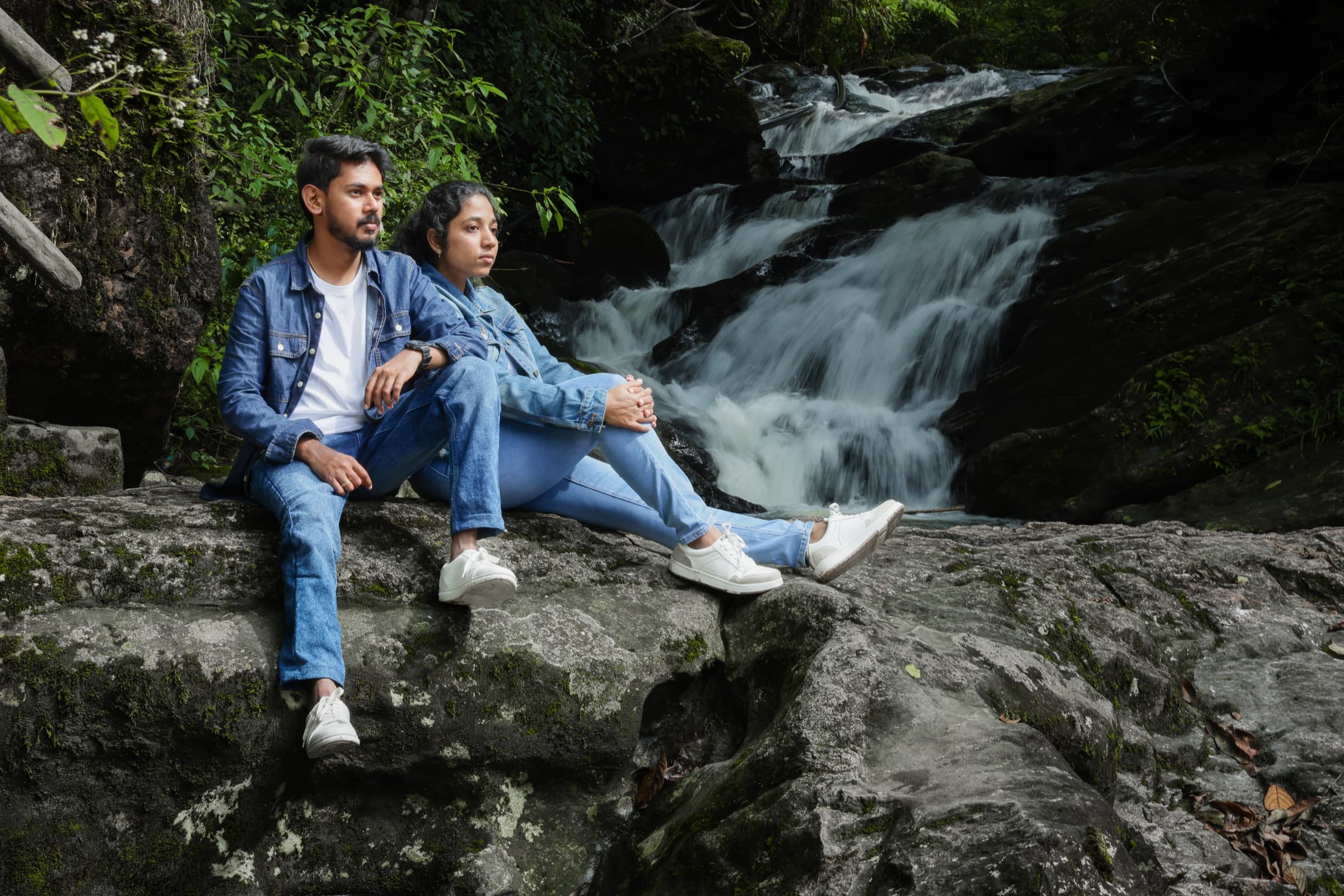 Couple seated on rocks beside a waterfall for a pre-wedding shoot